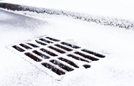 Metal drain grate covered with snow in winter.