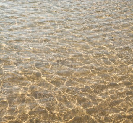 Téléchargez les photos : Surface de l'eau avec des ondulations et des reflets de rayons solaires. Eau peu profonde. Fond de sable. - en image libre de droit