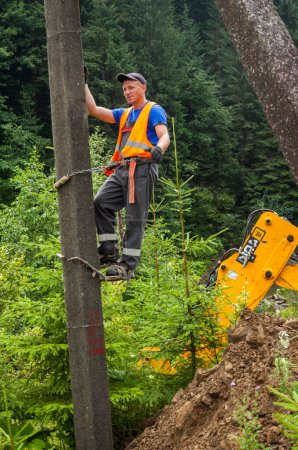 Photo for Ivano-Frankivsk region, Ukraine - August 16, 2021: Builder climbing the utility pole during the works on installation of the new utility poles along the rode in the Ukrainian Carpathians. - Royalty Free Image