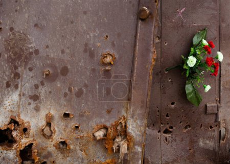 Irpin, Kyiv region, Ukraine -  April 12, 2022: Russian invasion of Ukraine. Bullet holes in the metal door of the residential building. Traces of shelling and fire. Bunch of flowers in the door.