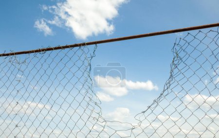 Téléchargez les photos : Clôture métallique cassée contre le ciel bleu. - en image libre de droit
