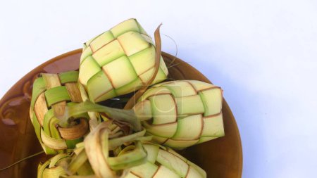 Ketupat (Reisknödel) auf Teller serviert isoliert weiß. Ketupat ist ein natürlicher Reismantel aus jungen Kokosblättern zum Kochen von Reis während des Eid Mubarak, Kopierraum