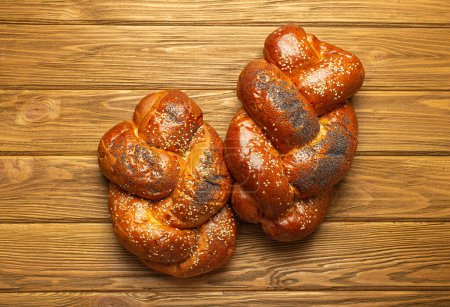 Photo for Two Freshly baked Challah bread covered with poppy and sesame seeds, top view on rustic wooden background, traditional festive Jewish cuisine. - Royalty Free Image