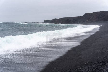 Ondas de lavado contra Djupalonssandur playa de arena negra en Islandia