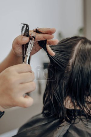 Gros plan des mains du coiffeur coupant les cheveux mouillés avec des ciseaux et un peigne.