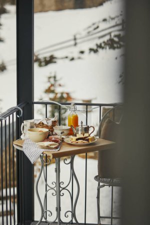 Cozy winter balcony breakfast with snowy hills backdrop.
