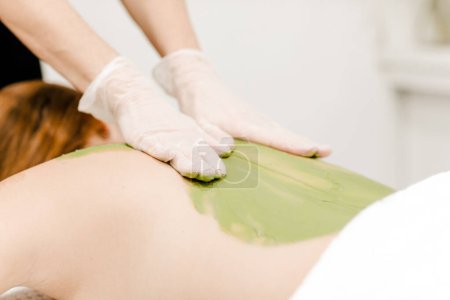 Foto de Mujer que recibe un masaje de espalda terapéutico con algas verdes, haciendo hincapié en la relajación y el tratamiento natural del cuidado de la piel - Imagen libre de derechos