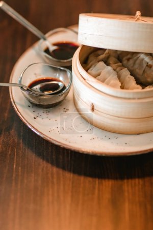 Detail shot of a dish featuring two small sauce containers beside a larger wooden bowl holding freshly made gyozas.