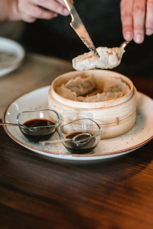 Photo for Detail shot of a dish featuring two small sauce containers beside a larger wooden bowl holding freshly made gyozas. - Royalty Free Image
