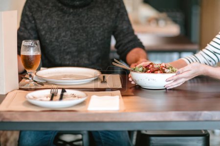 Téléchargez les photos : Serveuse servant une assiette de salade à un homme avec une bière à une table en bois dans un restaurant - en image libre de droit