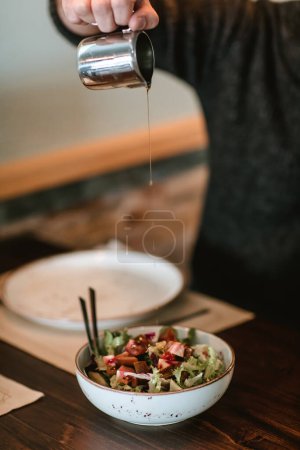 Photo for Close-up of a man pouring oil over a salad, capturing the precision and freshness of the dish - Royalty Free Image