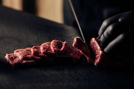 Primer plano de un chef con guantes negros rebanando carne de forma experta, mostrando precisión e higiene culinaria
