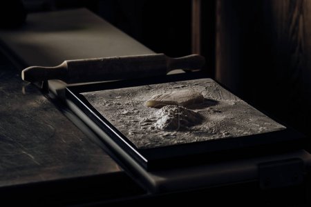 Photo for Restaurant kitchen table with a flour-filled tray, dough sprinkled with flour, and a rolling pin, ready for pastry making - Royalty Free Image