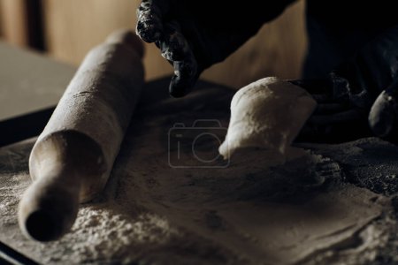 Hand in black gloves delicately shaping dough, showcasing meticulous culinary skill and care in food preparation