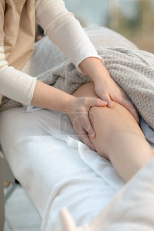 Téléchargez les photos : Gros plan sur un massage thérapeutique professionnel du genou dans un cadre de spa calme, en mettant l'accent sur les mains et la technique - en image libre de droit