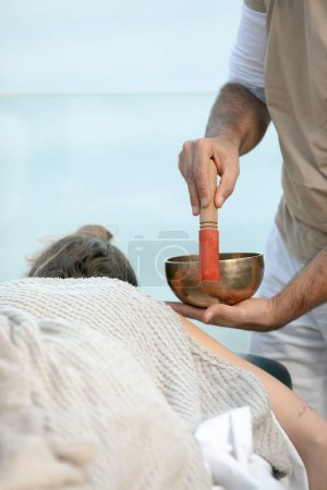 Holistic Wellness: Tibetan Singing Bowl Therapy Session by a Male Practitioner on a Female Client, Captured in a Serene Spa Environment