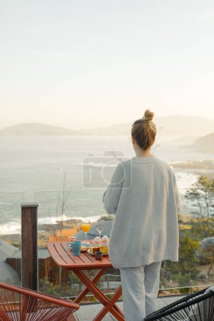 Morgendliche Gelassenheit: Frau genießt ein ruhiges Frühstück mit malerischem Meerblick von einer gemütlichen Terrasse