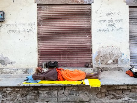Téléchargez les photos : Pushkar, Rajasthan, India - November 2022: Portrait of an old  sadhu baba resting on the street of Pushkar in traditional saffron dress with white beard. - en image libre de droit
