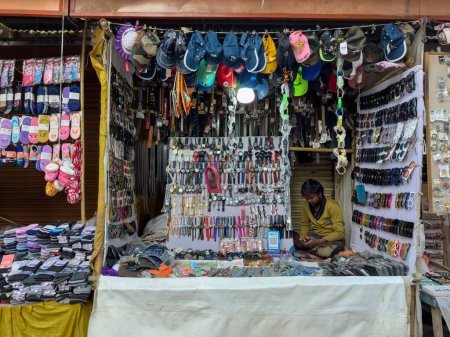 Foto de Pushkar, Rajastán, India - Noviembre 2022: Vendedor ambulante sentado fuera de la tienda en Pushkar. El mercado callejero de Pushkar es popular entre los lugareños y turistas por ropa y artículos tradicionales y étnicos.. - Imagen libre de derechos