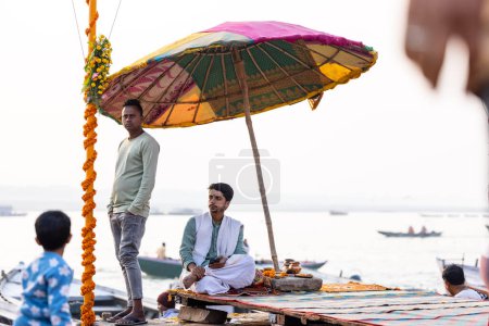 Téléchargez les photos : Varanasi, Uttar Pradesh, India - November 2022: Portrait of Unidentified Indian brahmin priest sitting under umbrella on ghat near river ganges in varanasi city. - en image libre de droit