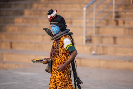 Téléchargez les photos : Varanasi, Uttar Pradesh, Inde - Novembre 2022 : Portrait d'un jeune garçon habillé comme Lord Shiva avec un visage bleu peint près de la rivière Ganges ghat dans la ville de Varanasi. - en image libre de droit