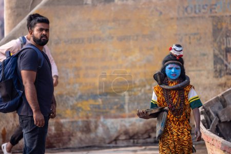 Foto de Varanasi, Uttar Pradesh, India - Noviembre 2022: Retrato de un joven vestido como Lord Shiva con la cara pintada de azul cerca de las pandillas del río ghat en la ciudad de Varanasi. - Imagen libre de derechos