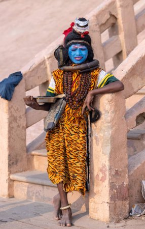Téléchargez les photos : Varanasi, Uttar Pradesh, Inde - Novembre 2022 : Portrait d'un jeune garçon habillé comme Lord Shiva avec un visage bleu peint près de la rivière Ganges ghat dans la ville de Varanasi. - en image libre de droit