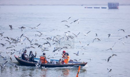 Téléchargez les photos : Varanasi, Uttar Pradesh, India - November 2022: Tourists enjoying boat side in the river ganges along with the herd of sea gulls at varanasi. - en image libre de droit