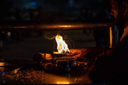 Foto de Rishikesh, Uttarakhand, India - October 2022: Portrait of hindu male priest performing river Gange aarti with fire flame in hand at triveni ghat to worship river ganges. Ganga aarti performed in night - Imagen libre de derechos