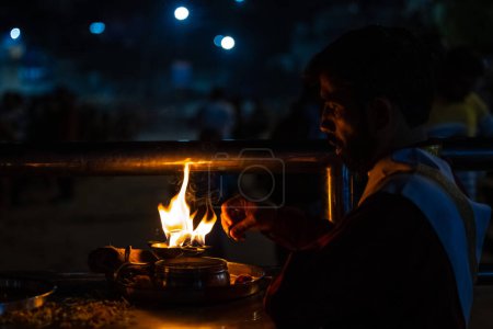 Foto de Rishikesh, Uttarakhand, India - October 2022: Portrait of hindu male priest performing river Gange aarti with fire flame in hand at triveni ghat to worship river ganges. Ganga aarti performed in night - Imagen libre de derechos