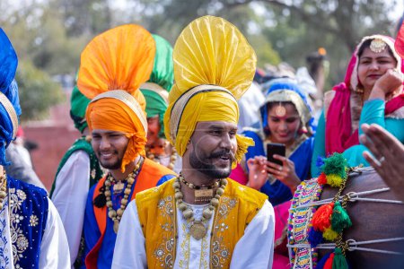 Foto de Bikaner, Rajasthan, India - January 2023: Punjabi Bhangra, Portrait of young sikh male in traditional punjabi colorful dress and turban performing bhangra dance with smile in camel festival with focus - Imagen libre de derechos