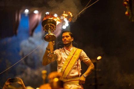 Téléchargez les photos : Varanasi, Uttar Pradesh, Inde - Novembre 2022 : Ganga aarti, Portrait d'un jeune prêtre exécutant des aarti du soir au ghat de dasasaswamedh en costume traditionnel avec des rituels hindous sanatan. - en image libre de droit