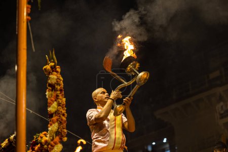 Foto de Varanasi, Uttar Pradesh, India - Noviembre 2022: Ganga aarti, Retrato de un joven sacerdote realizando bandas fluviales aarti vespertino en dasasaswamedh ghat con vestimenta tradicional con rituales hindúes sanatán. - Imagen libre de derechos