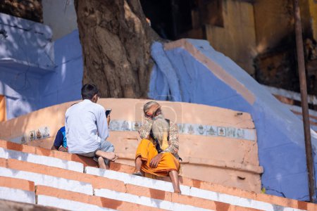 Foto de Varanasi, Uttar Pradesh, India - Noviembre 2022: Retrato de sadhu baba indio no identificado sentado en las escaleras - Imagen libre de derechos