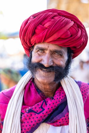 Foto de Pushkar, Rajastán, India - Noviembre 2022: Feria de Pushkar, Retrato de un hombre viejo rajasthani con vestido tradicional blanco y turbante colorido en el recinto ferial de pushkar. - Imagen libre de derechos