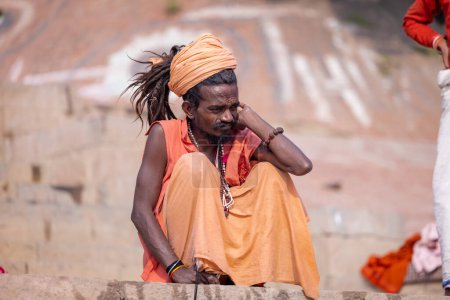 Foto de Varanasi, Uttar Pradesh, India - Noviembre 2022: Retrato de sadhu baba indio no identificado sentado en el ghat assi cerca de las pandillas fluviales en la ciudad de varanasi con vestimenta tradicional. - Imagen libre de derechos