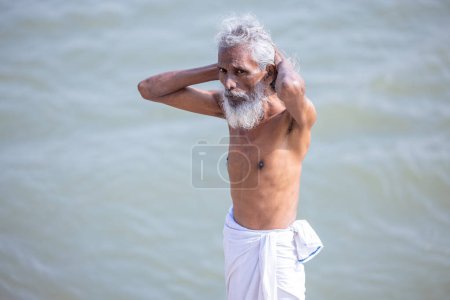 Téléchargez les photos : Varanasi, Uttar Pradesh, Inde - Novembre 2022 : Portrait d'un vieux sadhu mâle non identifié se tenant près de la rivière Ganges pendant le lever du soleil pour prendre un bain sacré dans la rivière Ganges comme rituels hindous. - en image libre de droit