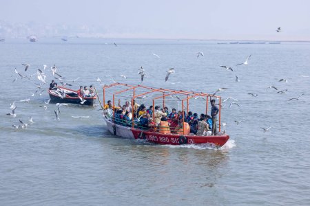 Téléchargez les photos : Varanasi, Uttar Pradesh, Inde - Novembre 2022 : Les touristes profitent d'une promenade en bateau dans les chaînes fluviales avec le troupeau de goélands marins à varanasi tôt le matin. Bateau naviguant sur le bateau en bois. - en image libre de droit