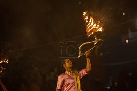 Téléchargez les photos : Varanasi, Uttar Pradesh, Inde - Novembre 2022 : Ganga aarti, Portrait d'un jeune prêtre exécutant des aarti de soirée sur la rivière Ganges à assi Ghat en costume traditionnel avec flamme de feu et rituels. - en image libre de droit