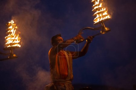 Foto de Varanasi, Uttar Pradesh, India - Noviembre 2022: Ganga aarti, Retrato de un joven sacerdote realizando pandillas fluviales aarti en assi Ghat con vestimenta tradicional con llama de fuego y rituales. - Imagen libre de derechos
