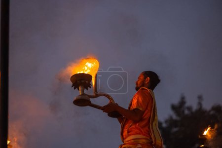 Téléchargez les photos : Varanasi, Uttar Pradesh, Inde - Novembre 2022 : Ganga aarti, Portrait d'un jeune prêtre exécutant des aarti de soirée sur la rivière Ganges à assi Ghat en costume traditionnel avec flamme de feu et rituels. - en image libre de droit