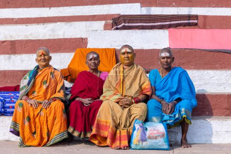 Téléchargez les photos : Varanasi, Uttar Pradesh, Inde - 20 novembre 2022 : Groupe de vieilles femmes sud-indiennes avec la tête rasée assis sur des escaliers au kedar ghat dans le saree traditionnel. tête chauve est rituel effectué en kashi. - en image libre de droit
