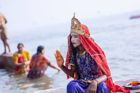 Photo for Varanasi, Uttar Pradesh, India - November 20 2022: Portrait of a young kid dress up like goddess parvati with painted face at kedar ghat riding in wooden boat in river ganges. - Royalty Free Image