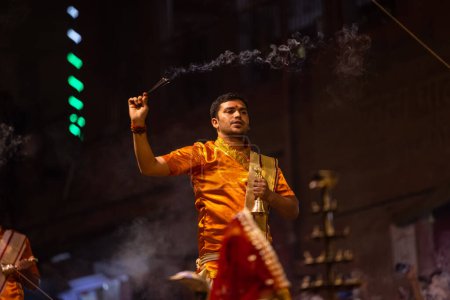 Foto de Varanasi, Uttar Pradesh, India - 20 de noviembre de 2022: Ganga aarti, Retrato del joven sacerdote realizando pandillas del río santo aarti vespertino en dashashwamedh ghat con vestimenta tradicional con rituales hindúes. - Imagen libre de derechos