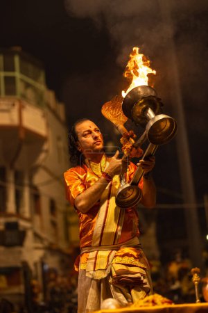 Foto de Varanasi, Uttar Pradesh, India - 20 de noviembre de 2022: Ganga aarti, Retrato del joven sacerdote realizando pandillas del río santo aarti vespertino en dashashwamedh ghat con vestimenta tradicional con rituales hindúes. - Imagen libre de derechos