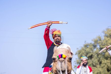 Téléchargez les photos : Bikaner, Rajasthan, Inde - 13 janvier 2023 : Festival du chameau, Portrait d'un jeune homme rajasthani avec barbe et moustache portant une robe traditionnelle blanche rajasthani et turban à dos de chameau. - en image libre de droit