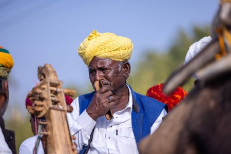 Téléchargez les photos : Bikaner, Rajasthan, Inde - 13 janvier 2023 : Festival du chameau, Portrait d'un vieil artiste rajasthani jouant de l'instrument de musique avec un turban coloré portant une robe rajasthani colorée traditionnelle. - en image libre de droit