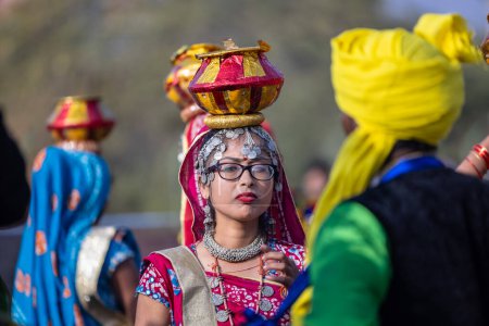 Foto de Bikaner, Rajastán, India - Enero13 2023: Festival del Camello Bikaner, Retrato de una joven hermosa con un vestido tradicional rajastaní sosteniendo una olla de barro en su cabeza mientras participaba en el desfile. - Imagen libre de derechos