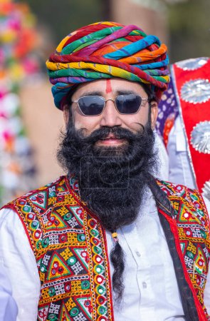 Téléchargez les photos : Bikaner, Rajasthan, Inde - 13 janvier 2023 : Festival du chameau, Portrait d'un jeune homme rajasthani avec barbe et moustache portant une robe traditionnelle blanche rajasthani et turban chevauchant sur un chariot à chameau. - en image libre de droit