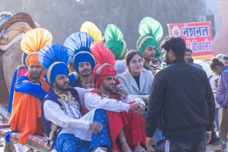 Foto de Bikaner, Rajastán, India - Ene 13 2023: Punjabi Bhangra, Retrato de un joven sikh masculino en el tradicional vestido de colores punjabi y turbante realizando danza bhangra con sonrisa en un festival de camellos con enfoque - Imagen libre de derechos